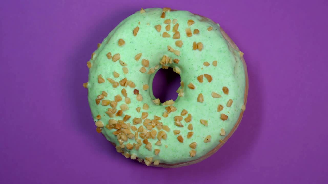 donut vidriado verde brillante con nueces en primer plano, macro disparado, girando sobre un fondo púrpura.