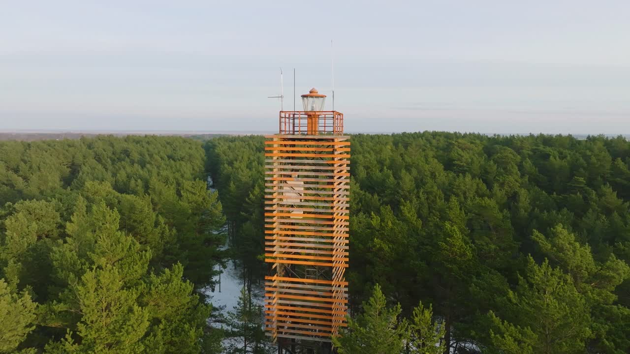 가벼운 눈, 북유럽 숲, 발트해 연안, 화창한 겨울날, 라트비아, 넓은 궤도를 도는 드론 샷이 있는 무성한 녹색 소나무 숲으로 둘러싸인 베르나티 등대의 공중 전망