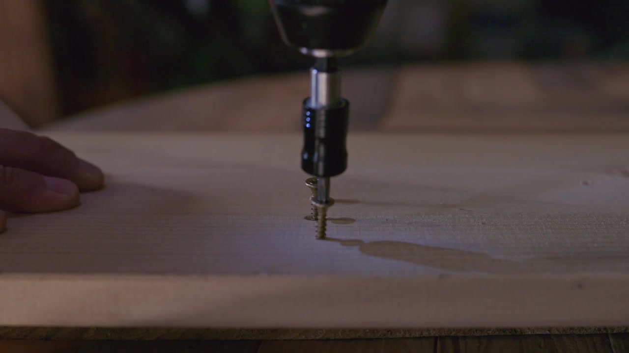 Primo piano di un trapano elettrico che avvita una vite in una tavola di legno, illustrando lavori di falegnameria, edilizia, fai da te e miglioramento della casa