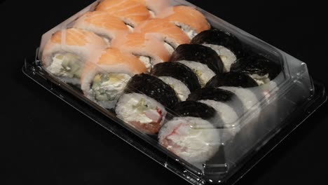 sushi rolls rotates in a plastic container on a black background. meal delivery