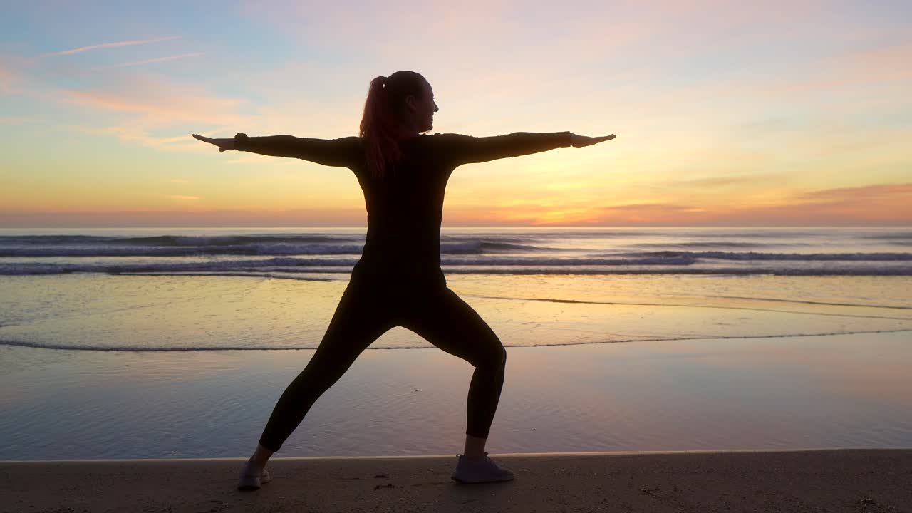 silueta de una mujer haciendo una pose de guerrero dos junto al mar durante el amanecer