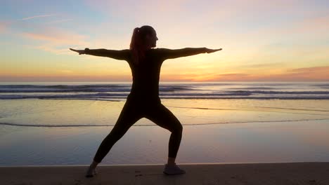 Silueta-De-Mujer-Haciendo-Pose-De-Guerrero-Dos-Junto-Al-Mar-Durante-El-Amanecer