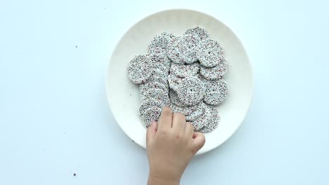 la mano alcanzando caramelos salpicados de colores en un plato