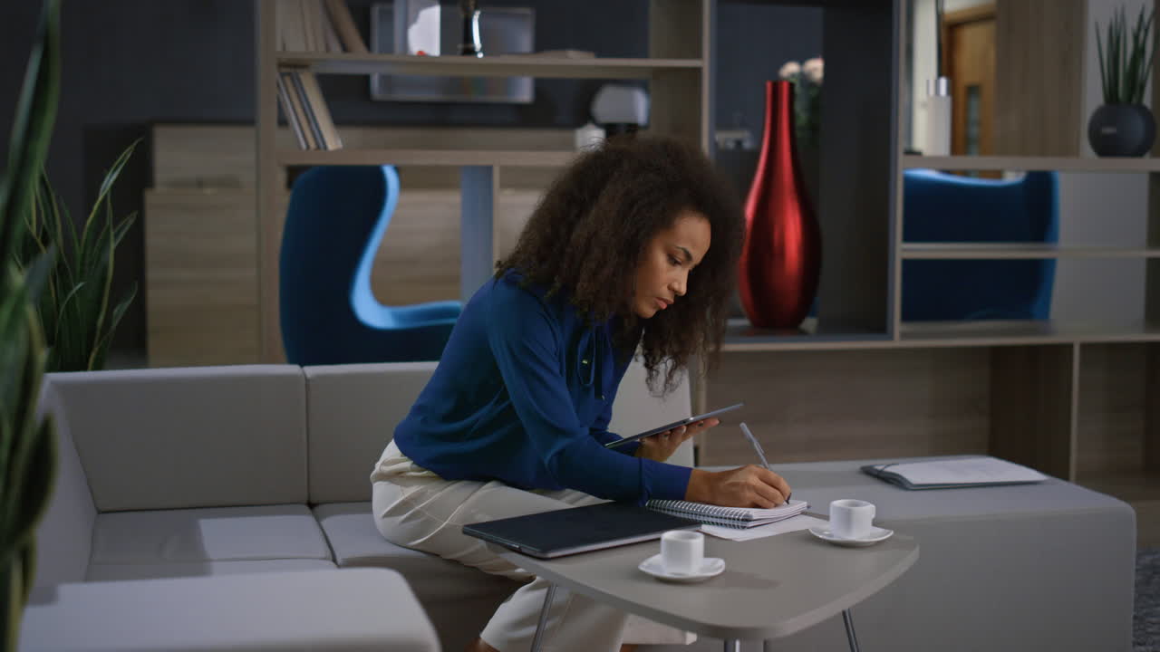 mujer de negocios afroamericana trabaja en una tableta y escribe notas en una videollamada en la oficina.