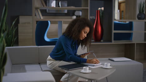 African-american-businesswoman-work-tablet-write-notes-on-video-call-in-office.