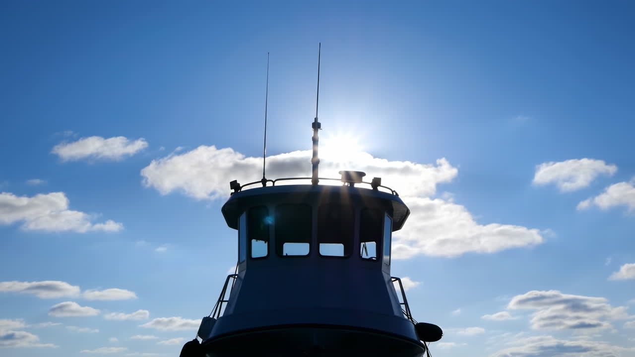 Silhouette del ponte di una nave contro il sole, timoneria retroilluminata con antenne e ringhiere, cielo azzurro brillante.