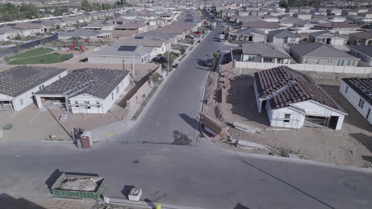 un avión no tripulado vuela graciosamente por una calle recién construida, revelando construcciones caseras parcialmente terminadas a lo largo del camino