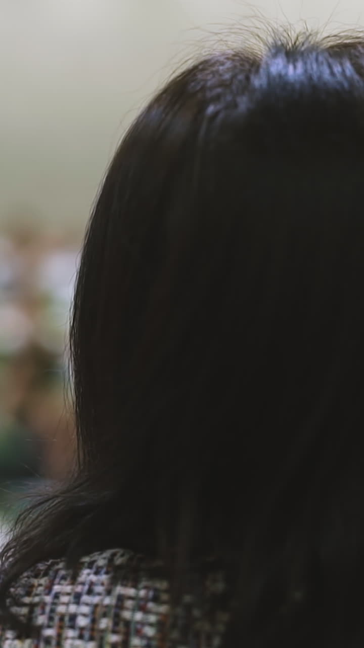 CU, slow motion: short haired brunette woman in jacket ready for haircut sits in armchair in modern brightly lit beauty salon backside close view
