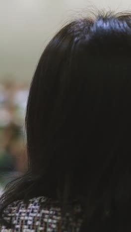 cu, slow motion: short haired brunette woman in jacket ready for haircut sits in armchair in modern brightly lit beauty salon backside close view
