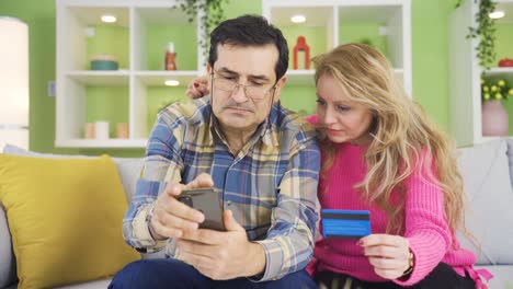 pareja usando un dispositivo de teléfono inteligente mientras están sentados en el sofá en una casa acogedora.