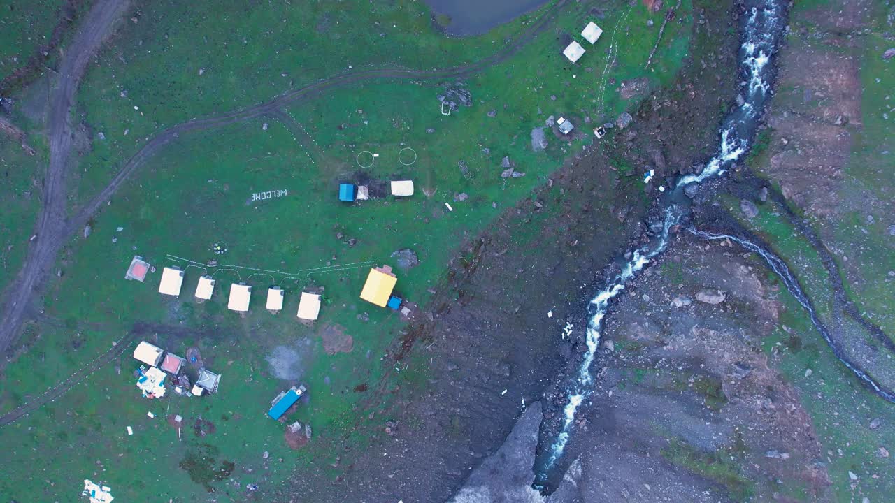 Drone shot of tents near a lake and mountain stream, set in a remote grassy highland area
