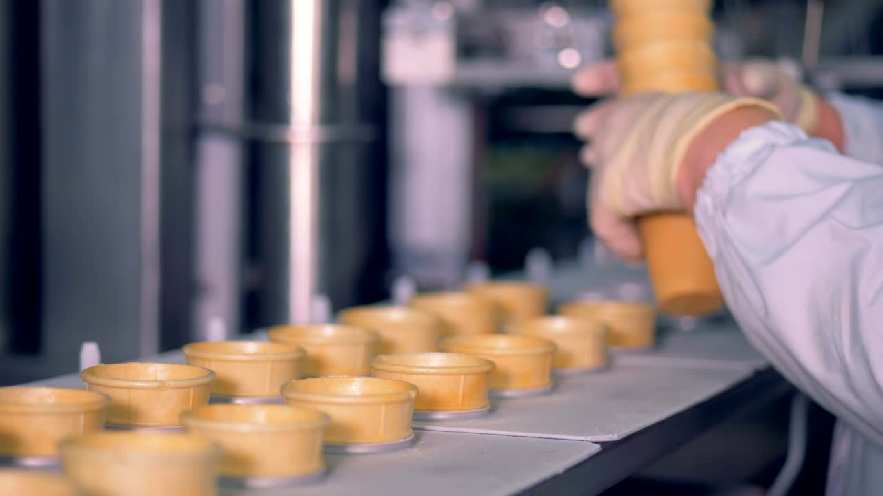 A pile of waffle cups is getting inserted into the conveyor belt by a factory worker