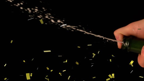 golden confetti falling over mid section of person spraying champagne against black background