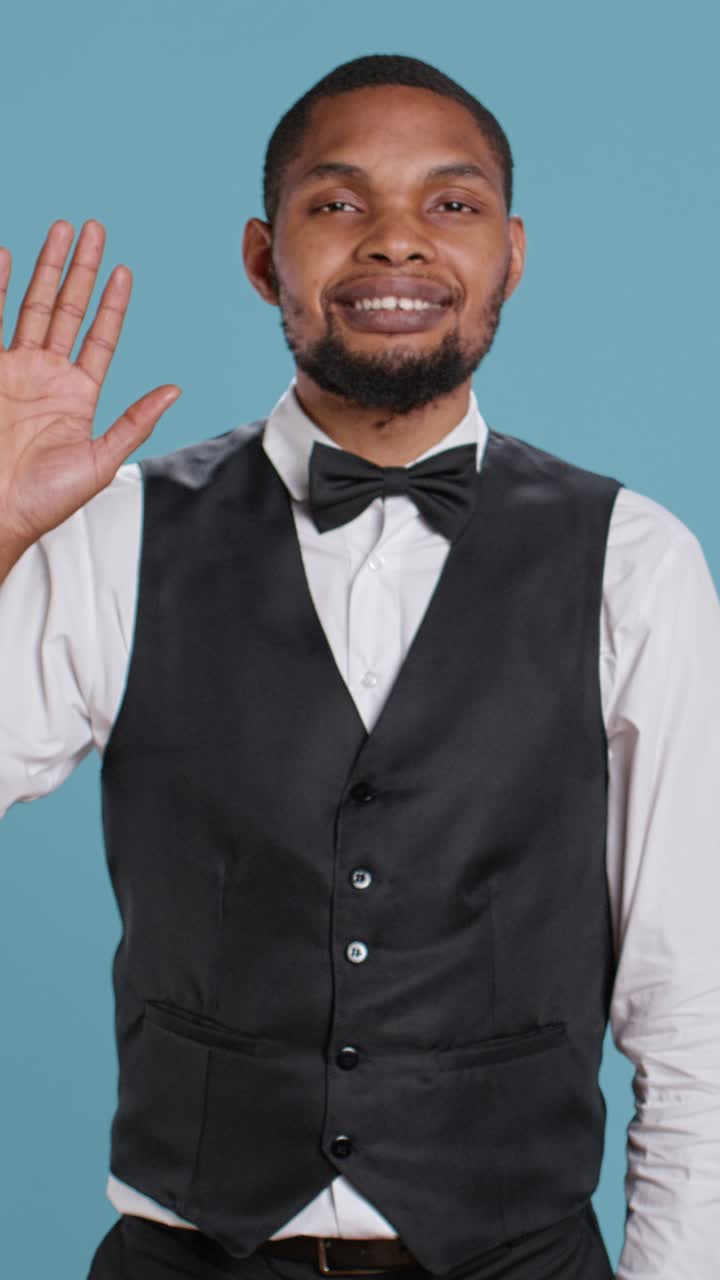 Cameriere sorridente e che saluta con la mano in uniforme formale