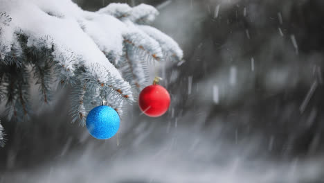 red and blue christmas balls hanging on a pine tree while it's snowing