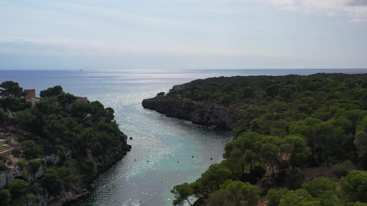 Spiaggia di Cala Pi con case sul mare sopra scogliere rocciose a Maiorca, Spagna, ripresa aerea in allontanamento
