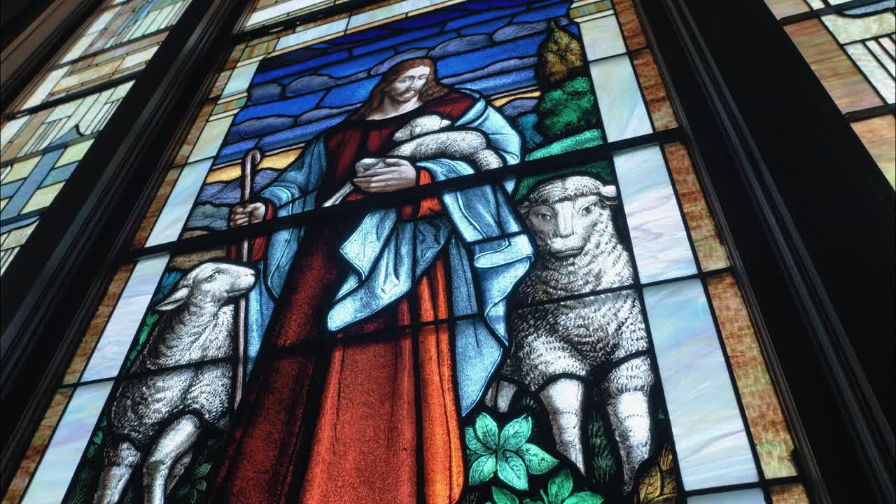 Religious stained-glass window with Jesus and sheep illuminates a church sanctuary, highlighting artistry, devotion, and sacred storytelling