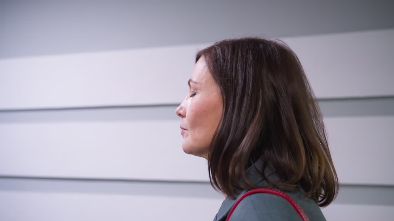 Close-up profile view of businesswoman walking in modern office hallway with sleek wall design. Professional appearance, focused expression, formal attire, and confident demeanor in corporate setting