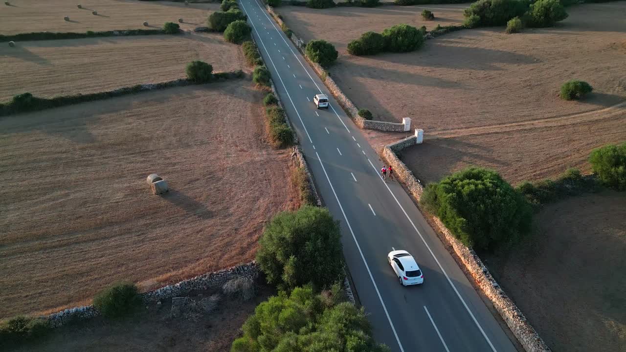 Cyclists pedal towards Platges des Fornells in Menorca, bathed in the warm glow of the setting sun, with the serene coastal landscape and peaceful evening light enhancing the ride.