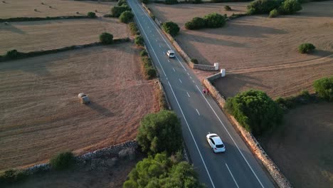 cyclists pedal towards platges des fornells in menorca, bathed in the warm glow of the setting sun, with the serene coastal landscape and peaceful evening light enhancing the ride.