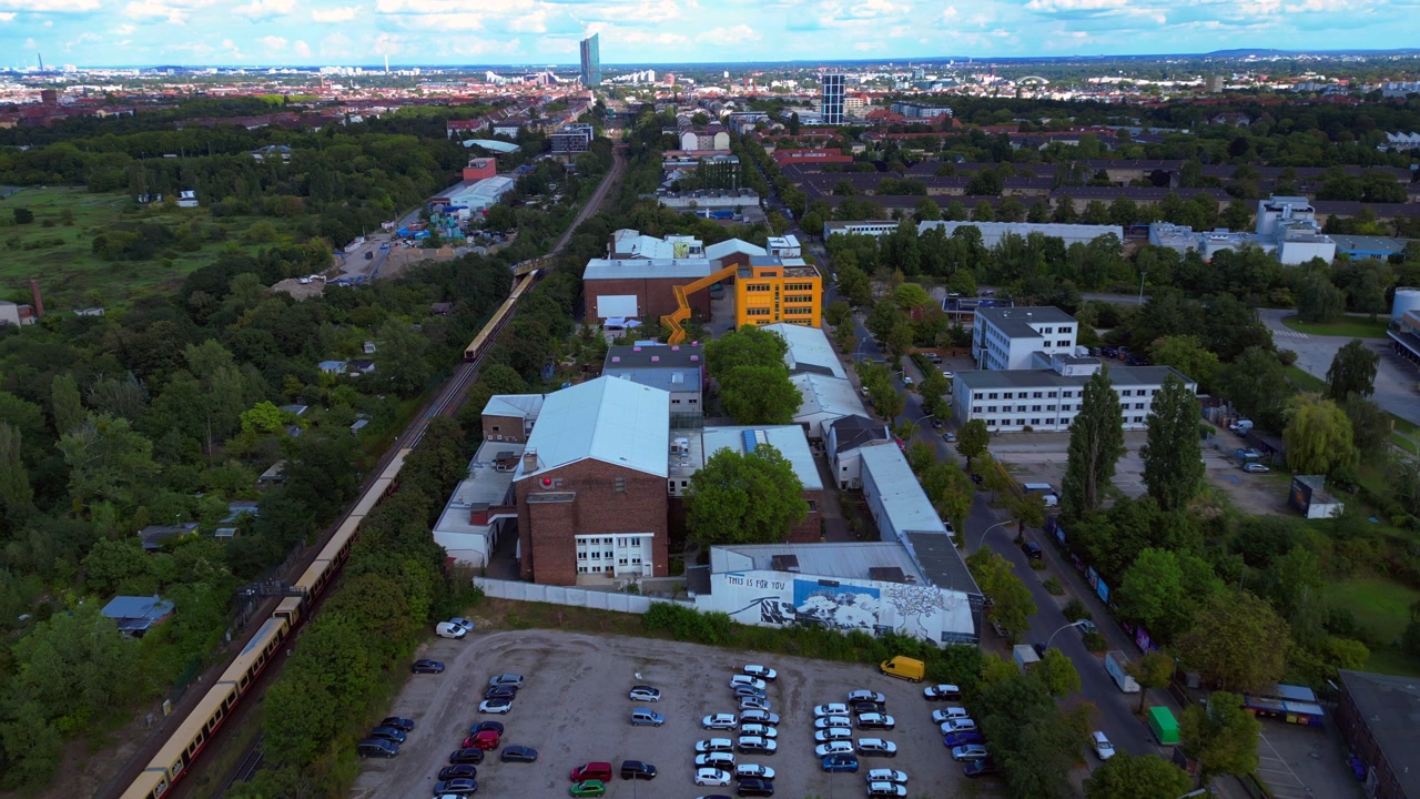yellow S Bahn train driving through Tempelhofer Feld in Berlin, Germany, on a sunny summer day. Smooth aerial view flight drone shot from above
