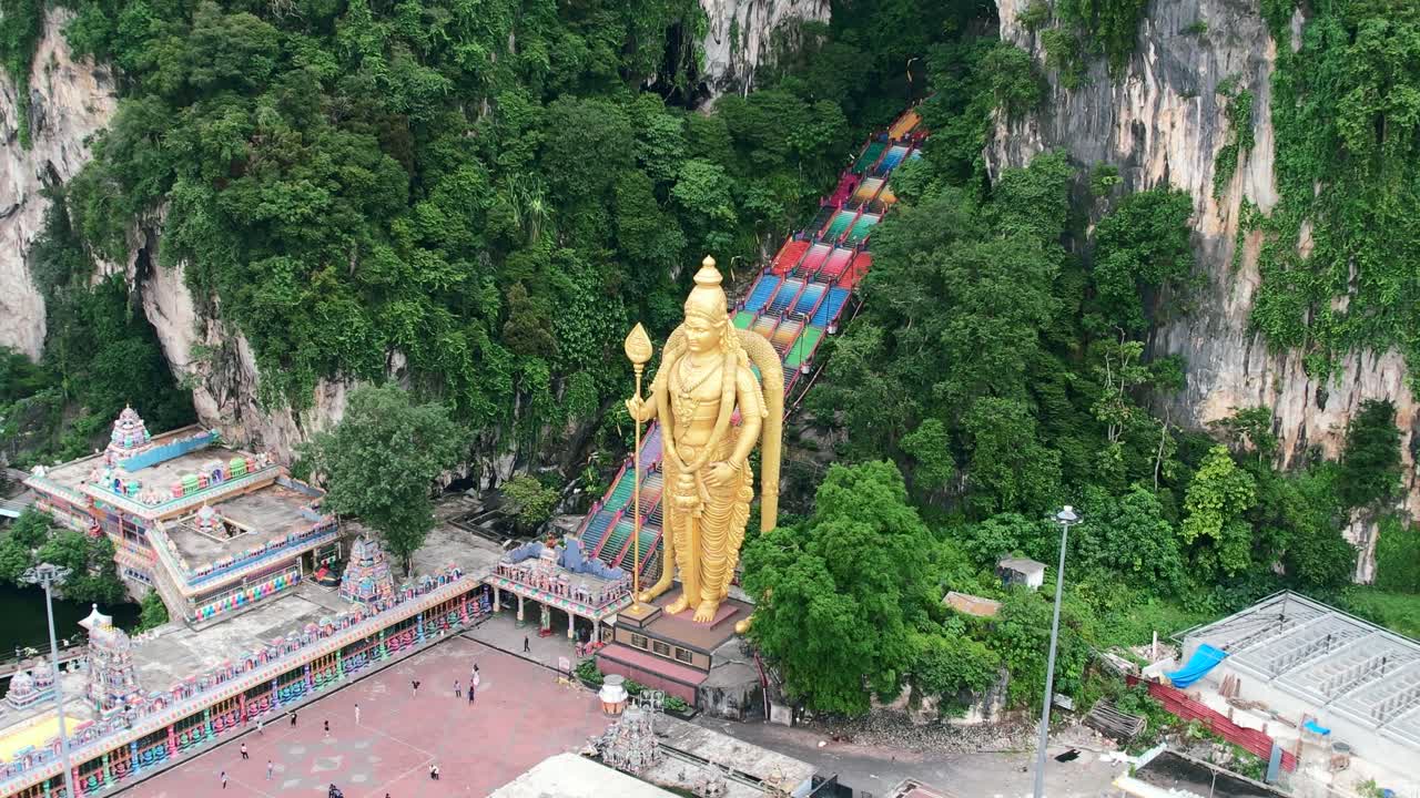 aerial drone circling the Lord Murugan statue with a colorful staircase leading to the Batu Caves in Kuala Lumpur Malaysia on a cloudy afternoon with no tourists