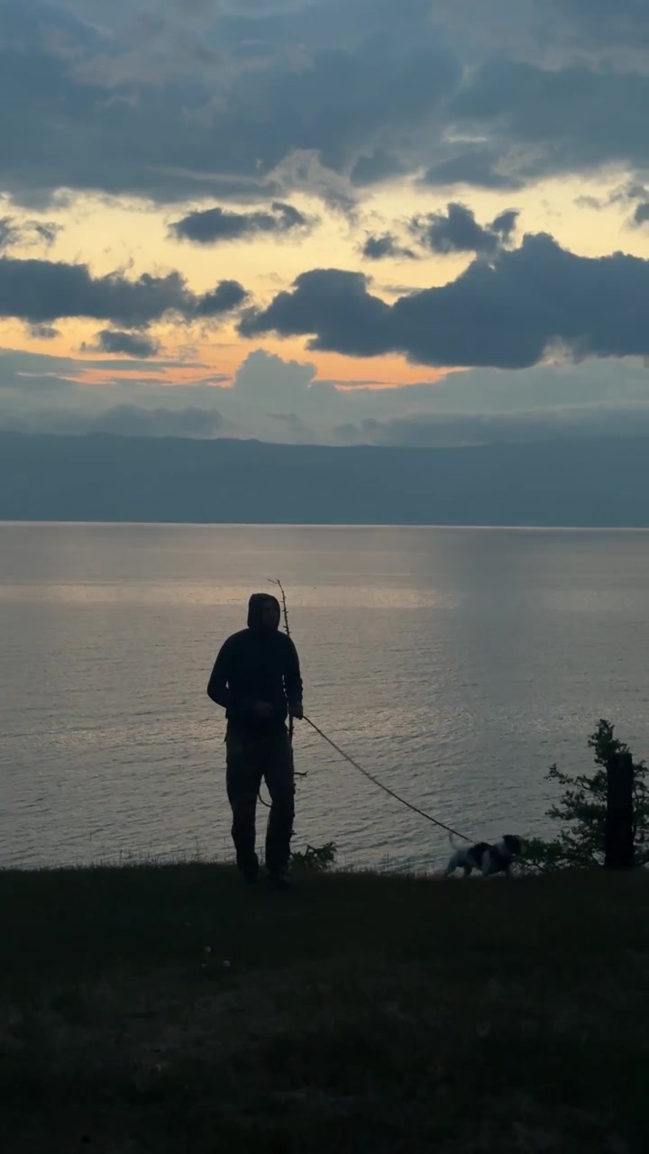 Seorang pria berjalan dengan anjingnya di sepanjang tepi Danau Baikal di Distrik Olkhonsky, Rusia saat matahari terbenam