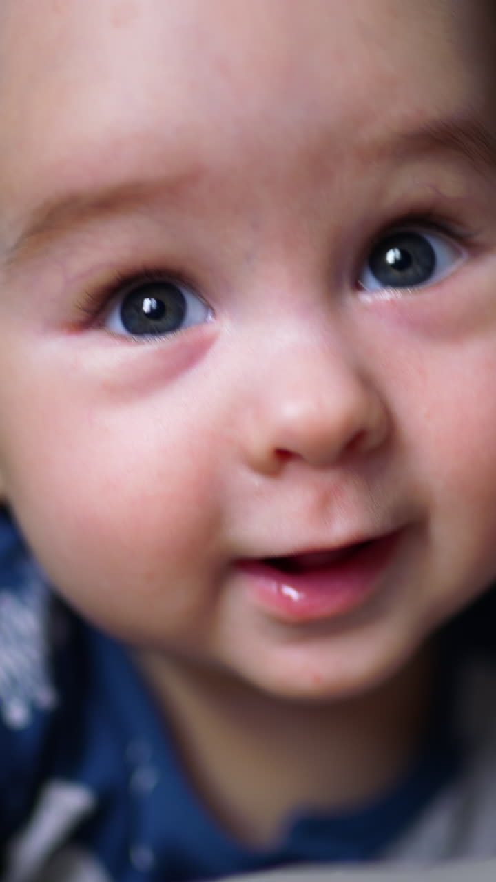 Beautiful Caucasian child lying on his belly. Baby boy in blue clothes smiles to the camera. Close up. Vertical video