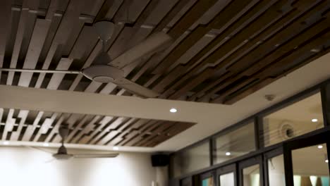 a ceiling fan rotates in a contemporary room with wooden slats and glass windows, creating a calm and airy atmosphere