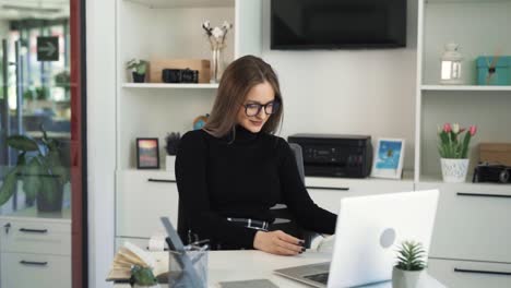 The-young-woman-is-sitting-at-a-table-in-front-of-a-laptop