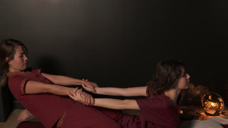 closeup view of a young woman having thai massage in spa by a female massagist in kimono. thai massagist is stretching the woman's back holding her hands. 4k shot