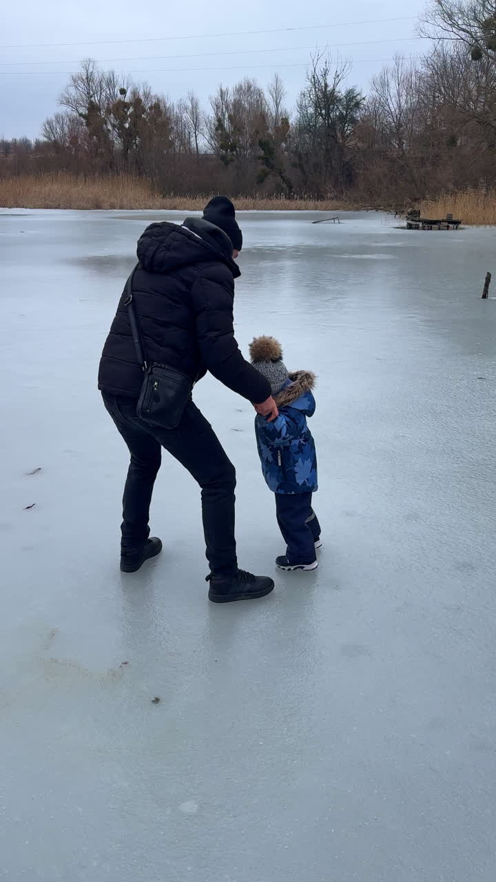 Far og søn er på vintertur på den frosne flod. Far støtter barnet, der glider på isen. Vertikal video.