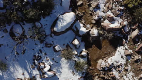 Drone-view-of-a-small-creek-flowing-down-on-a-snow-covered-mountain