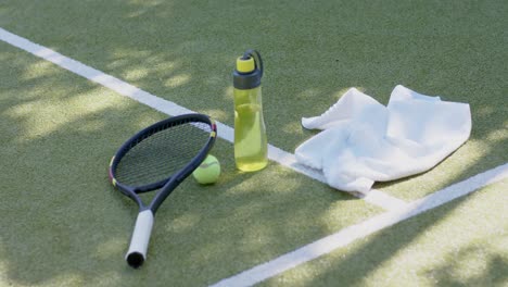raqueta de tenis, pelota de tenis, toalla y botella de agua en la cancha de tenis.