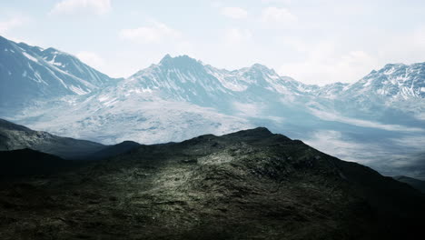 Aerial-Over-Valley-With-Snow-Capped-Mountains-In-Distance