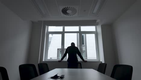 a man gazes out of the window from a conference room in an office setting, reflecting the solitary contemplation and decision-making process often found in the workplace