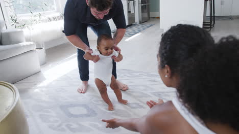 Parents-Encouraging-Smiling-Baby-Son-To-Take-First-Steps-And-Walk-At-Home