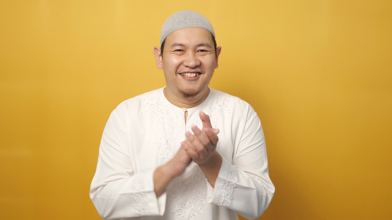 Happy proud Asian muslim man clapping gesture, half body portrait on yellow background