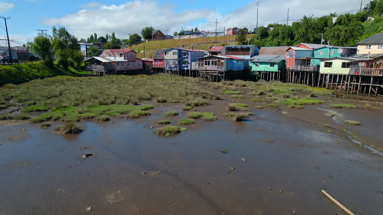 dolly en el establecimiento de un humedal con marea baja y coloridas palafitas en castro, chiloe, chile
