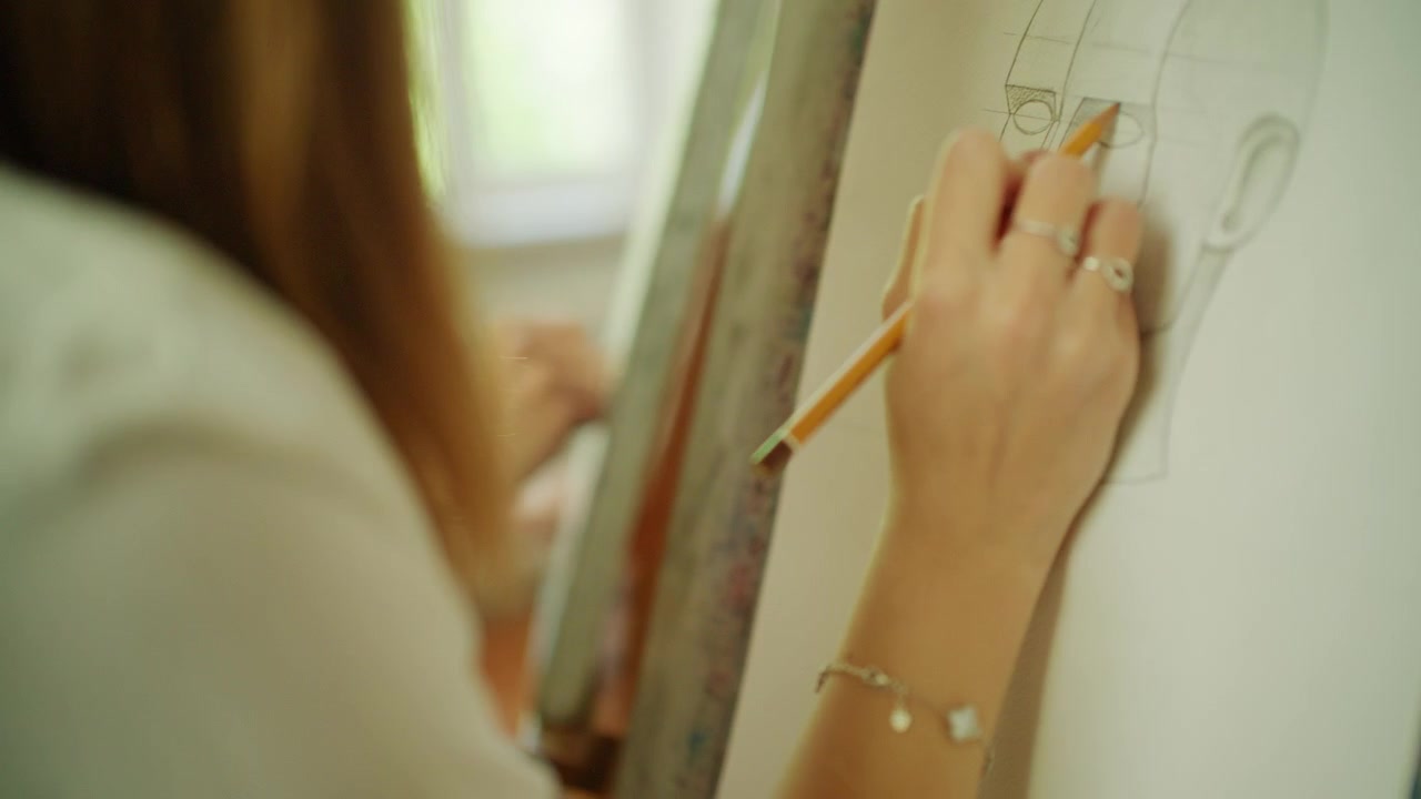Young art student drawing a portrait sketch on paper mounted on an easel during a classroom workshop