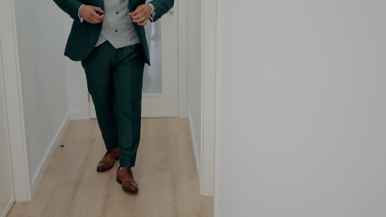 Brudgom i skreddersydd grønn dress og brune sko som går i en minimalistisk hvit gang.