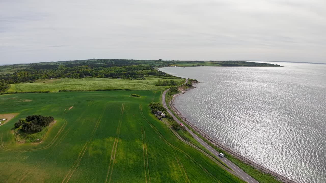 Dronefilmopptak fra luften av den danske kystlinjen nær Sletterhage, som viser grønne kystområder som møter rolig, blått hav under skyet himmel.