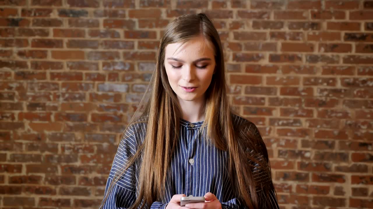 Young beautiful girl is watching her smartphone, thinking concept, communication concept, relaxing concept, brick background