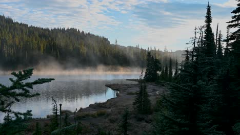aerial view of mist rising from a tranquil alpine lake bordered by dense evergreen forest