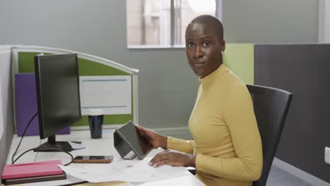 Portrait-of-happy-african-american-businesswoman-sitting-at-desk-in-office-in-slow-motion