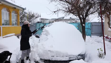 woman removes snow from car with snow brush - wide