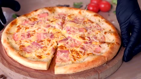 chef cuts a pizza with bacon and cheese on wooden board on the table.