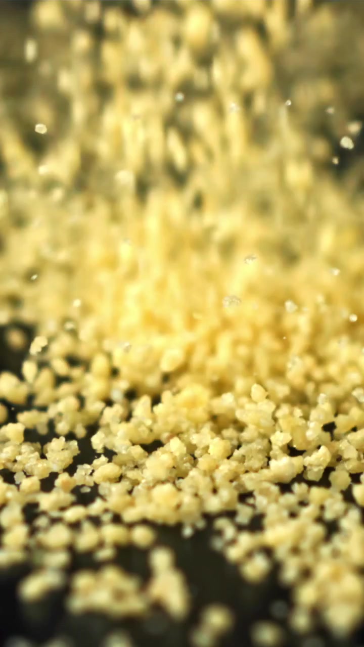 Primo piano di chicchi di couscous giallo che cadono su una superficie scura