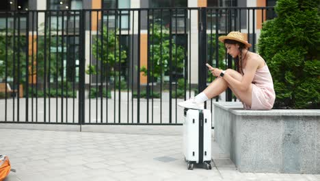 mujer con maleta usando un teléfono móvil al aire libre