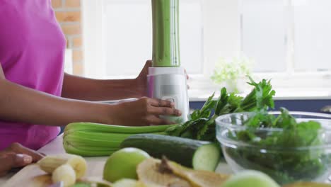 sección media de madre y hija afroamericanas preparando una bebida saludable en la cocina